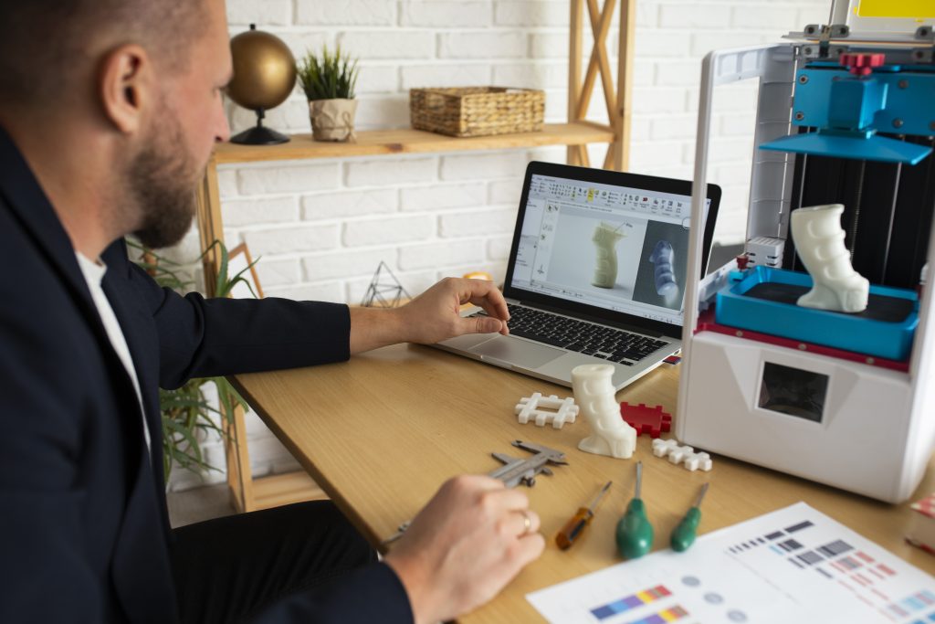 A man working on a computer, designing a book cover with creative tools and color palettes on the screen.