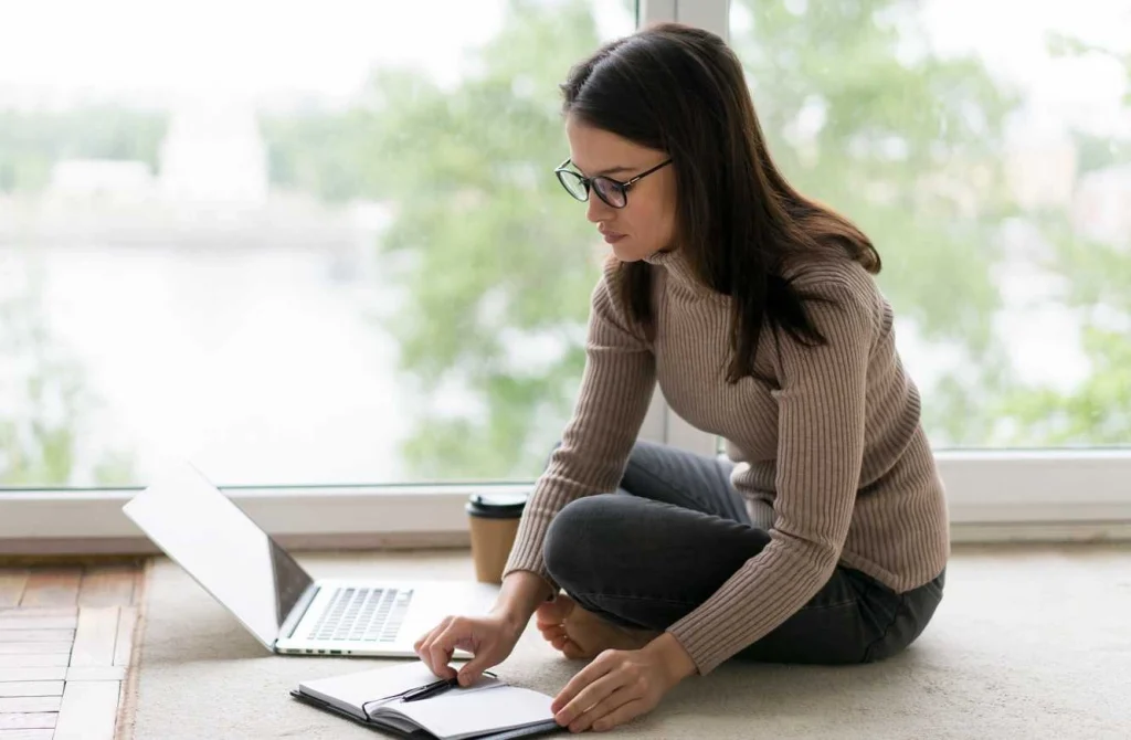 Woman working on laptop sitting on floor writing notes