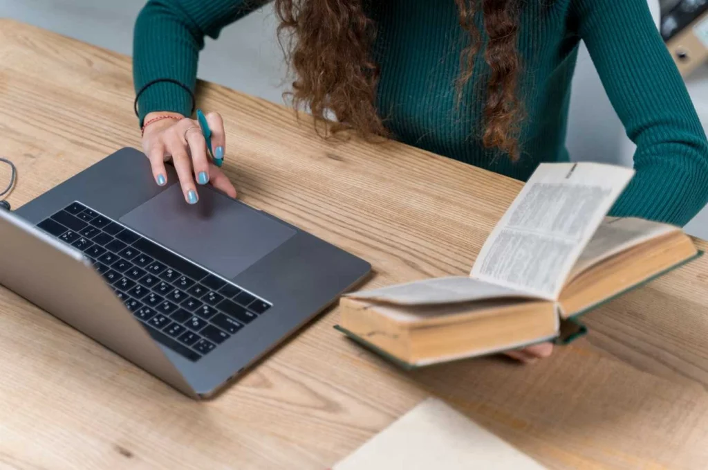 Close-up of woman reading book and using laptop