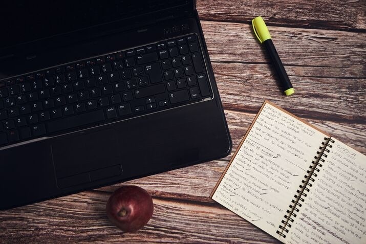 Laptop and open notebook on a wooden desk, representing proofreading and manuscript editing.