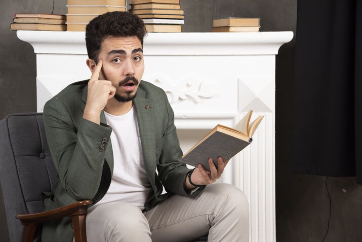 Man reading a book with a thoughtful expression, showing creative inspiration while writing or storytelling.