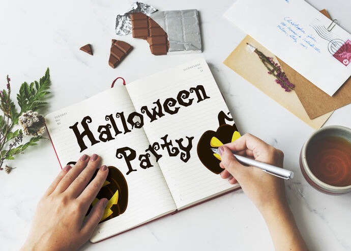 Person writing Halloween Party in a notebook while planning a spooky themed event.