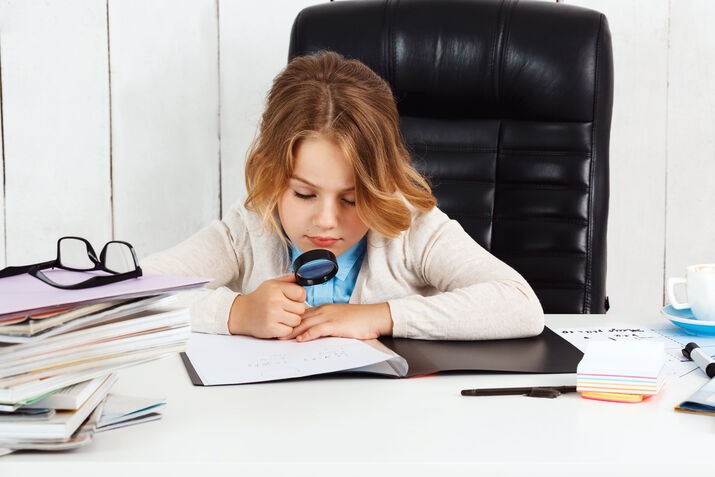 Young student using a magnifying glass to carefully proofread a written document.